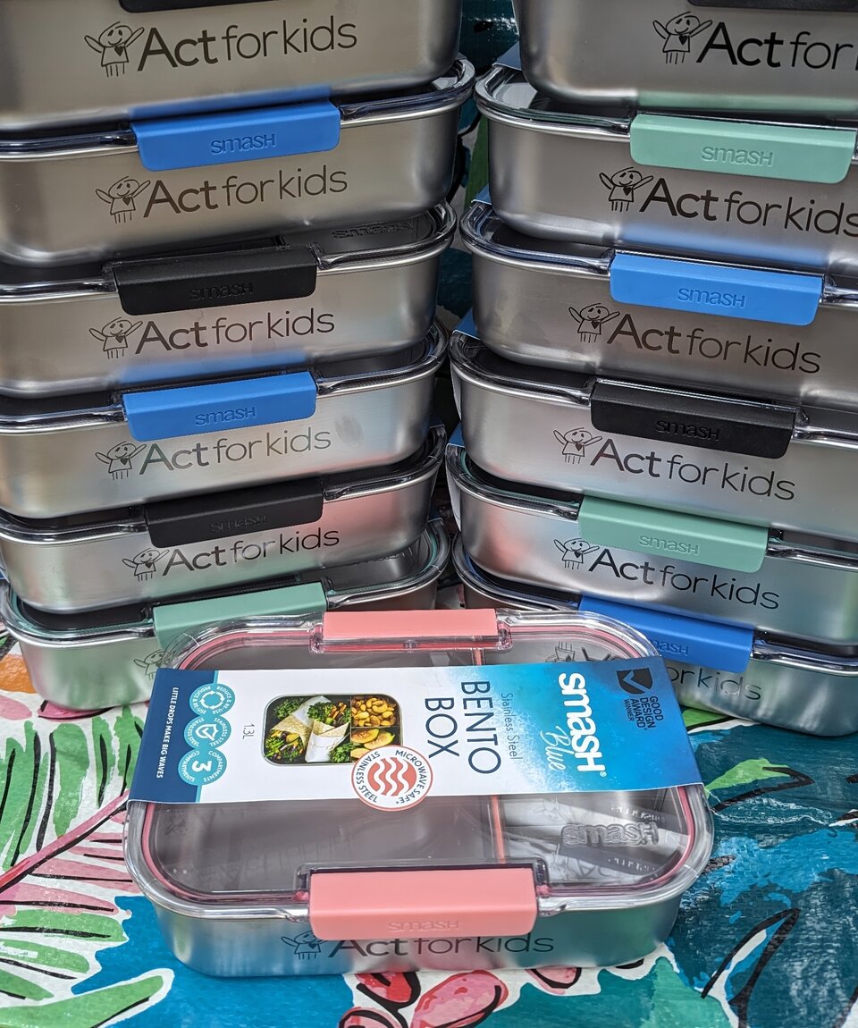 Stacked steel bento boxes, each with fiber etching on them reading "Act for kids"